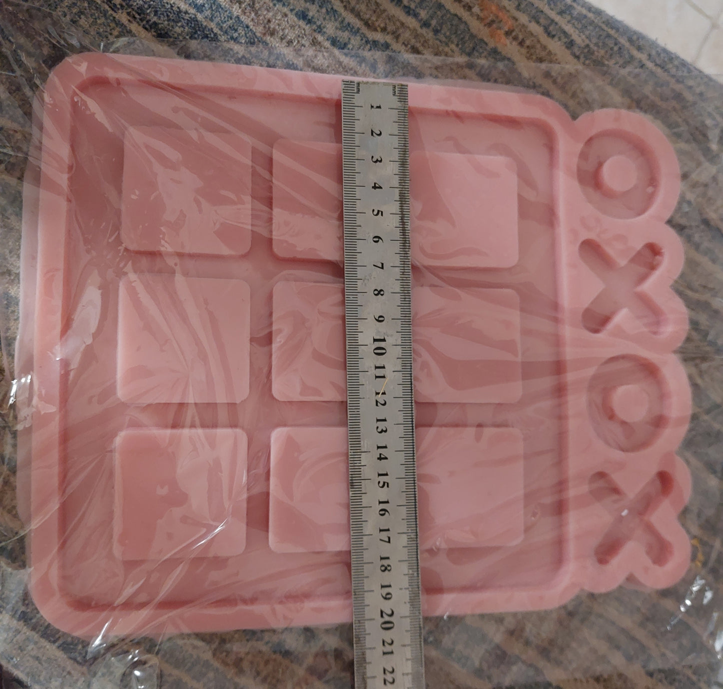 A silicone mold is a large square containing 9 raised squares arranged in a (3x3) grid, producing the basic game board for the game "Tic-Tac-Toe" with cavities for placing the pieces.
