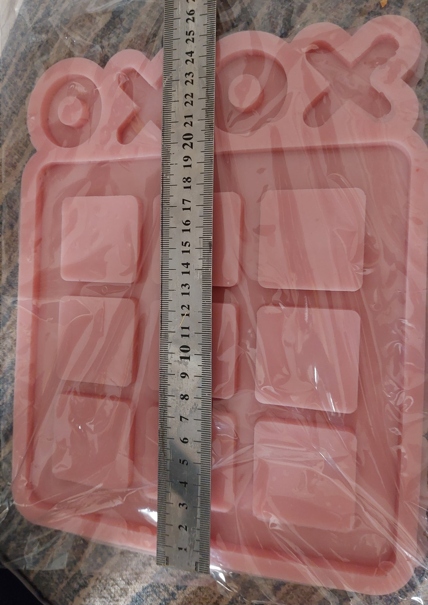 A silicone mold is a large square containing 9 raised squares arranged in a (3x3) grid, producing the basic game board for the game "Tic-Tac-Toe" with cavities for placing the pieces.