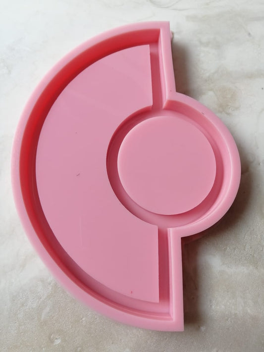 A silicone mold consists of a main cavity in the shape of a semicircle surrounding a complete circle in the center, with straight dividers separating the parts. It is used for casting resin, wax, or ceramics.