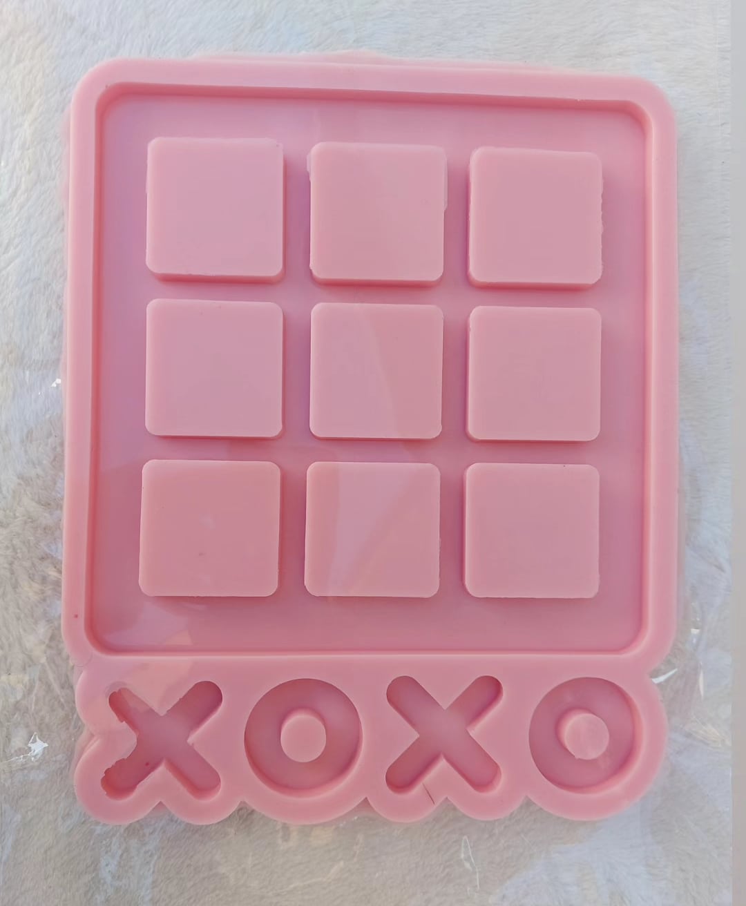 A silicone mold is a large square containing 9 raised squares arranged in a (3x3) grid, producing the basic game board for the game "Tic-Tac-Toe" with cavities for placing the pieces.